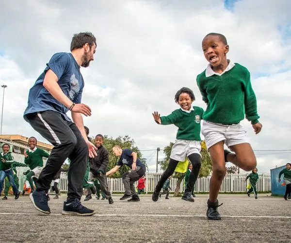 Volunteers playing a game in school yard with young children.