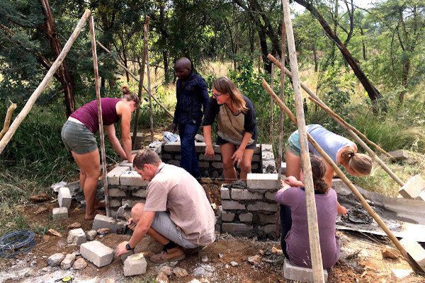 Team of volunteers building a structure together that is made from stones and bricks