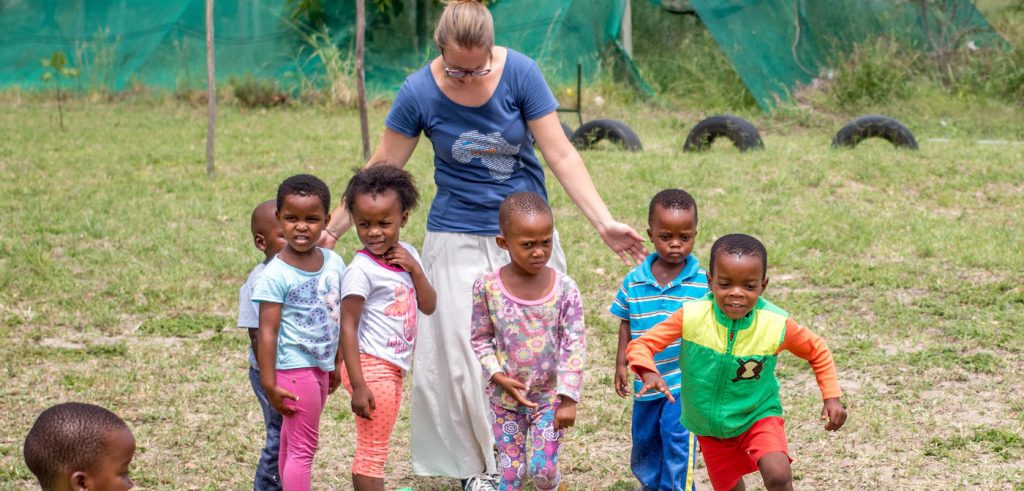 Volunteer at creche walking with young children in yard area.
