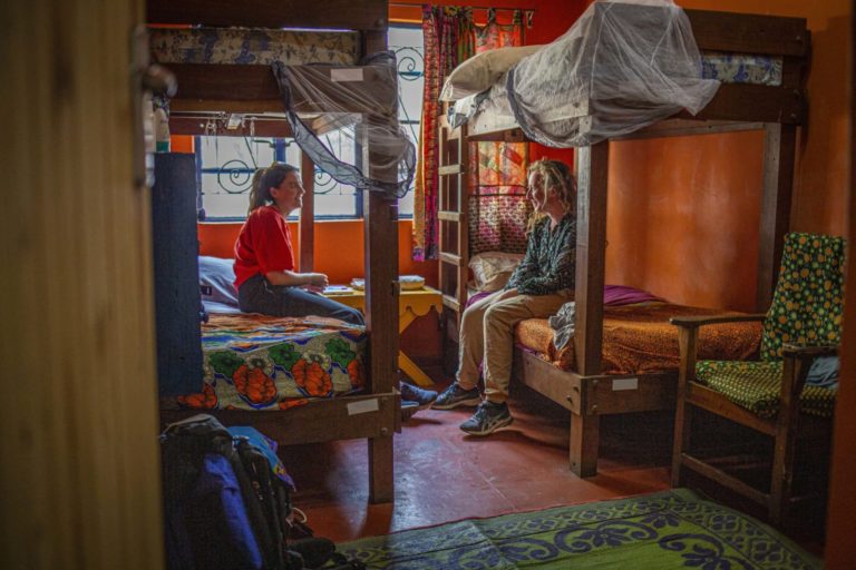 Two volunteers sitting on the lower bunks of two bunkbeds and talking in a colourful room at Victoria Falls Backpackers in Zambia