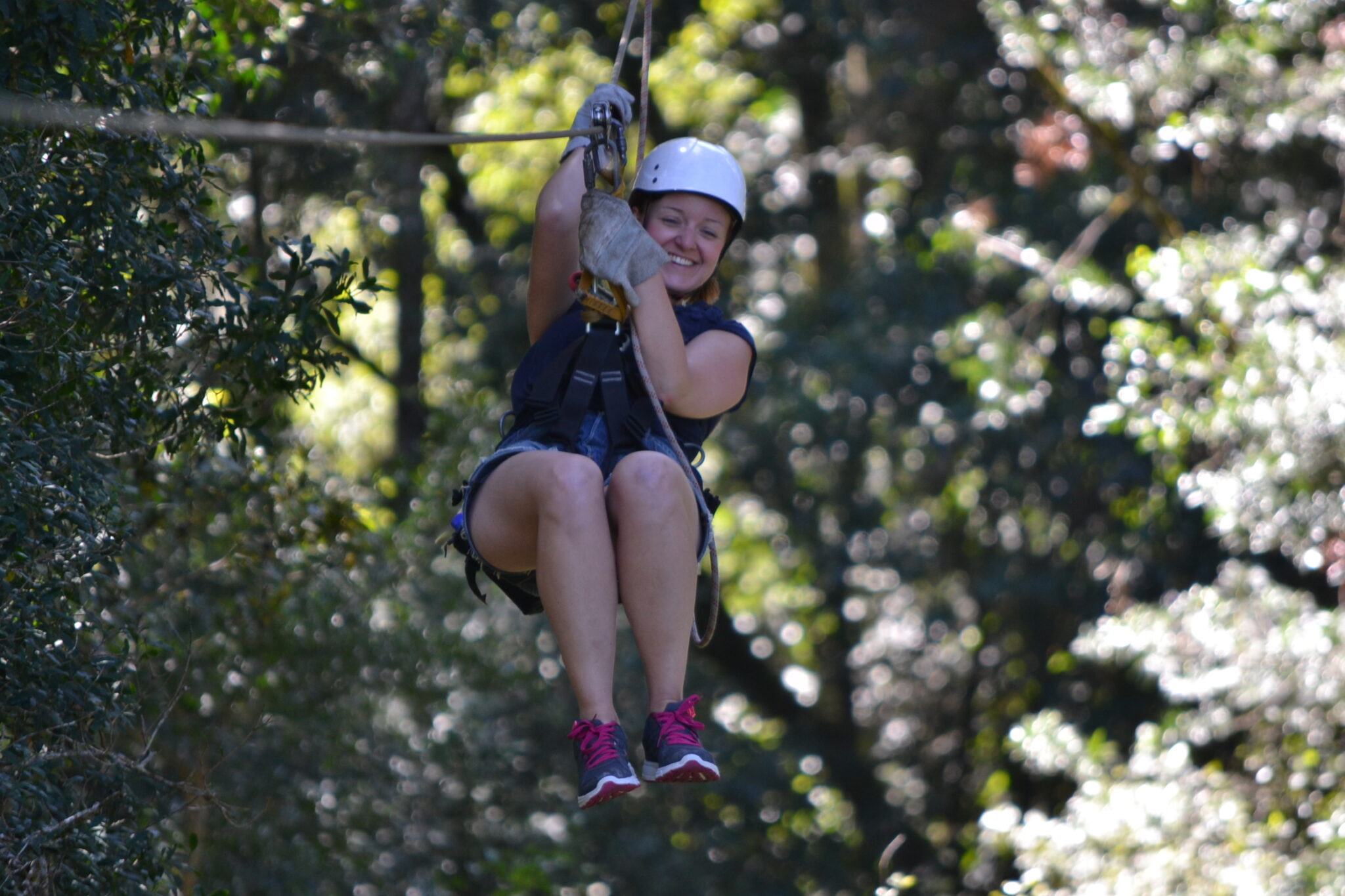 Happy volunteer smiling whilst ziplining in a forest.