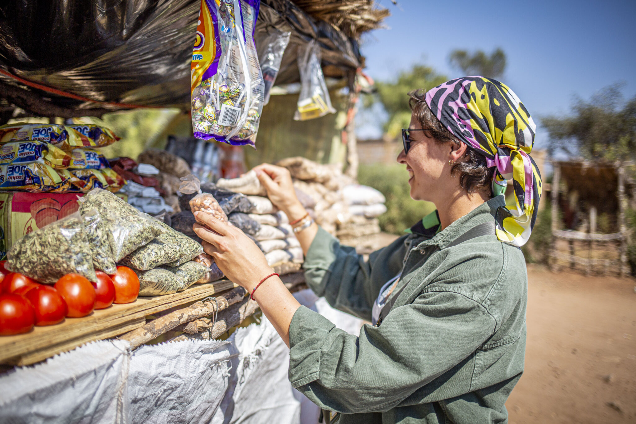 A woman in a colorful headscarf looking at the goods at a small roadside stall