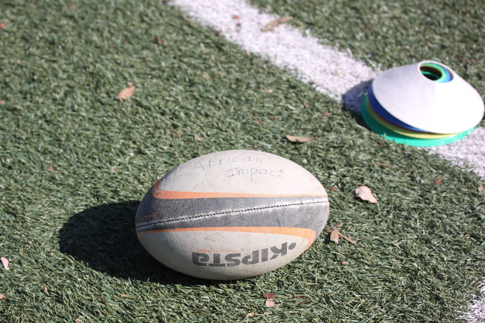 rugby ball against an astro turf floor with the words african impact written across the rugby ball