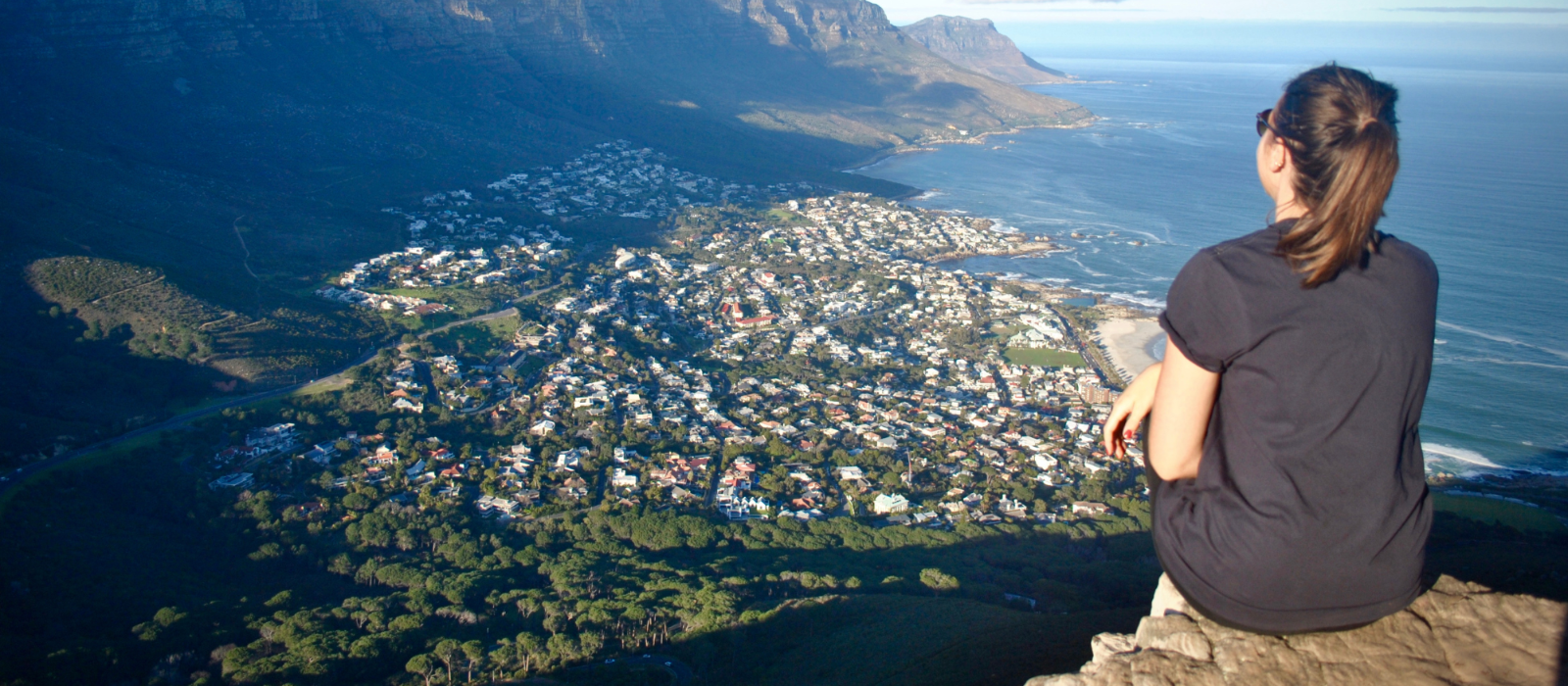 a woman sitting on a tip of a cliff with a view of South Africa