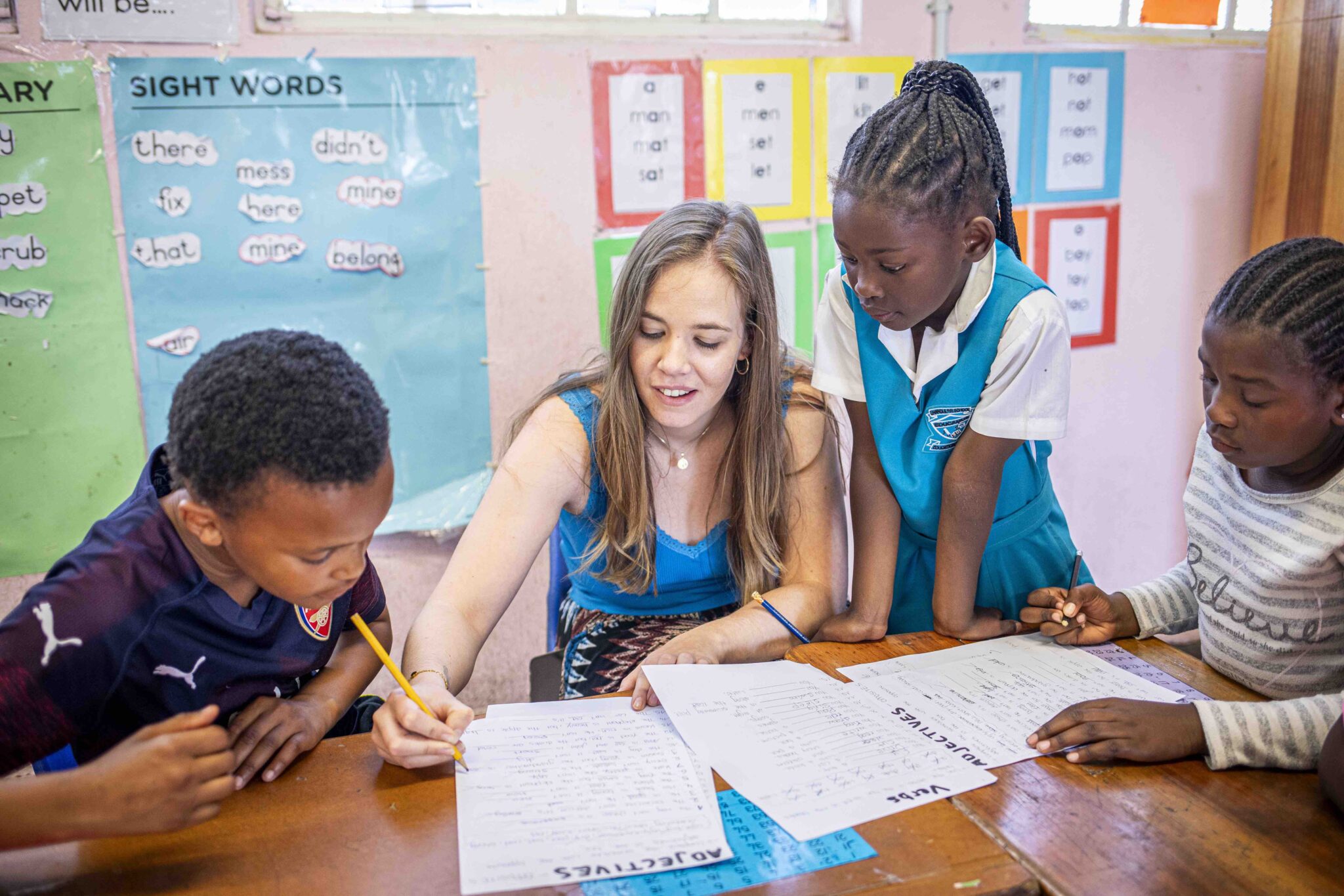 a woman volunteer writing on a paper and teaching young students