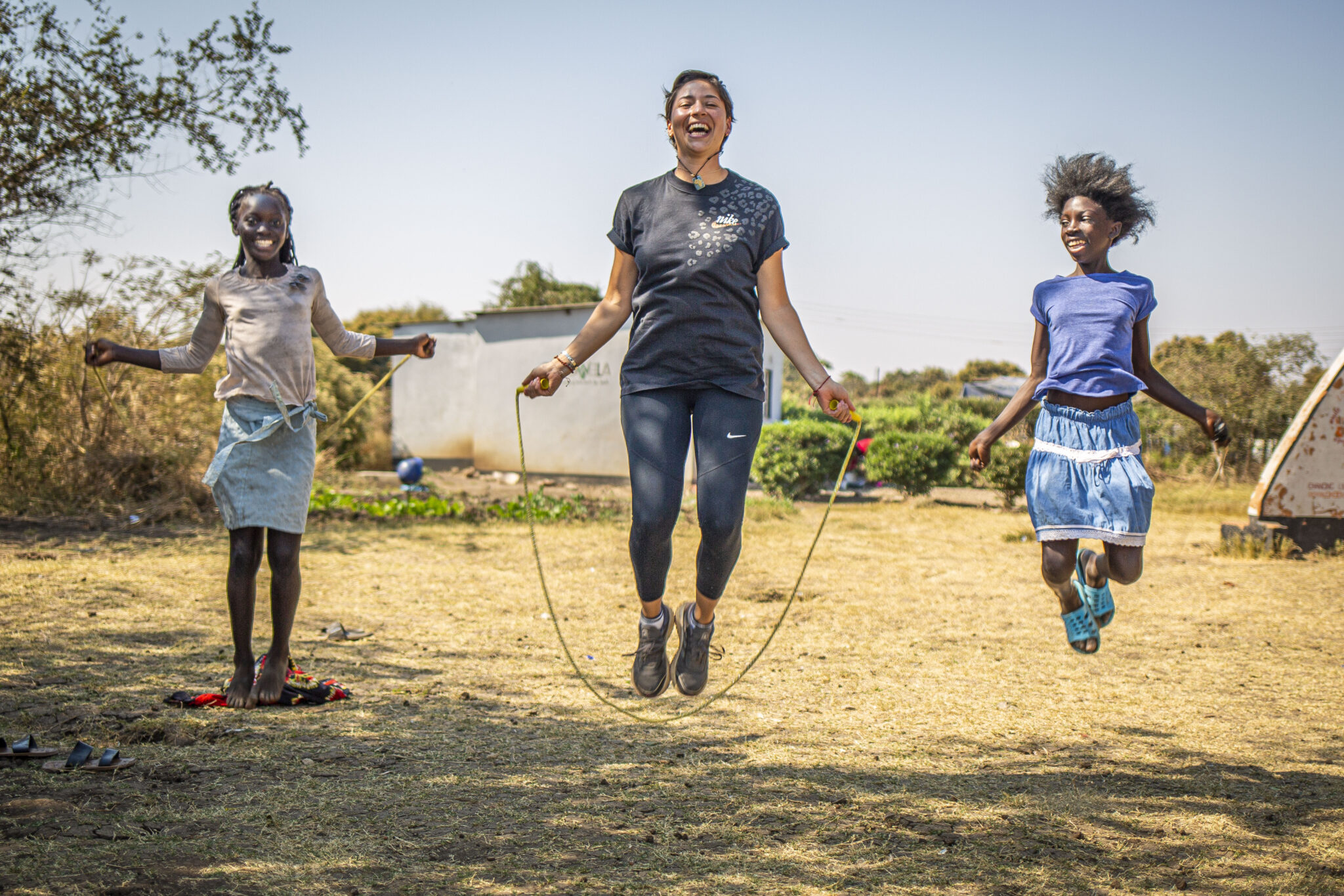 A foreign woman volunteer and two local young girls joyfully jumping rope together
