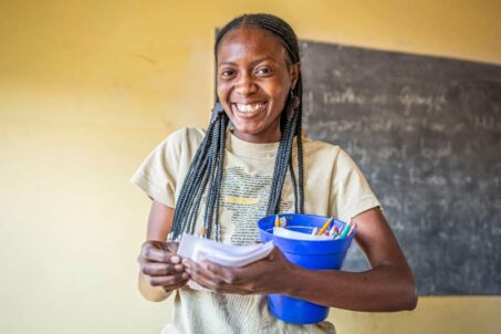 A Zambian woman smiling while holding paper and pens