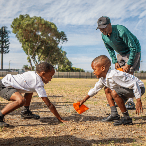 Two boys competing in a playful challenge during a sports activity, supervised by a coach