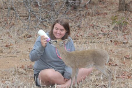 a woman kneeling down next to a deer