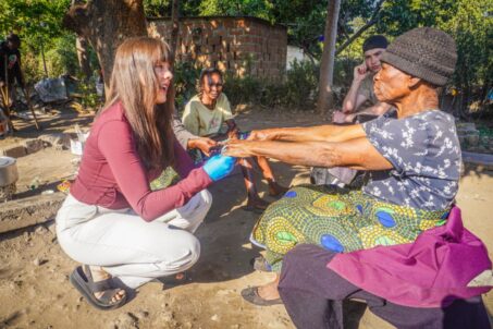Volunteer assisting elderly woman outdoors.