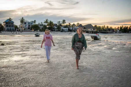 Two women stroll along the beach.